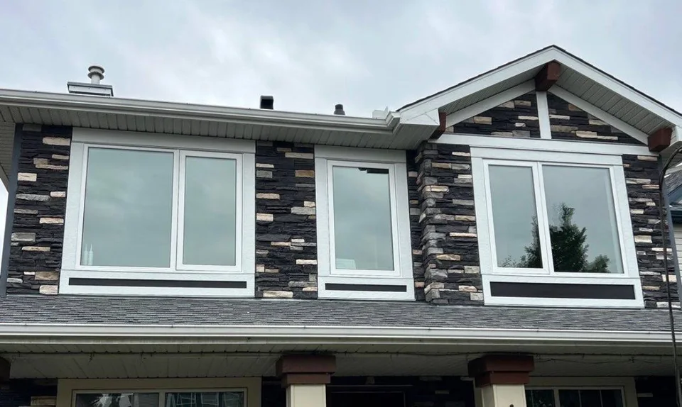 Completed upper façade with white-framed windows set into dark stone cladding.