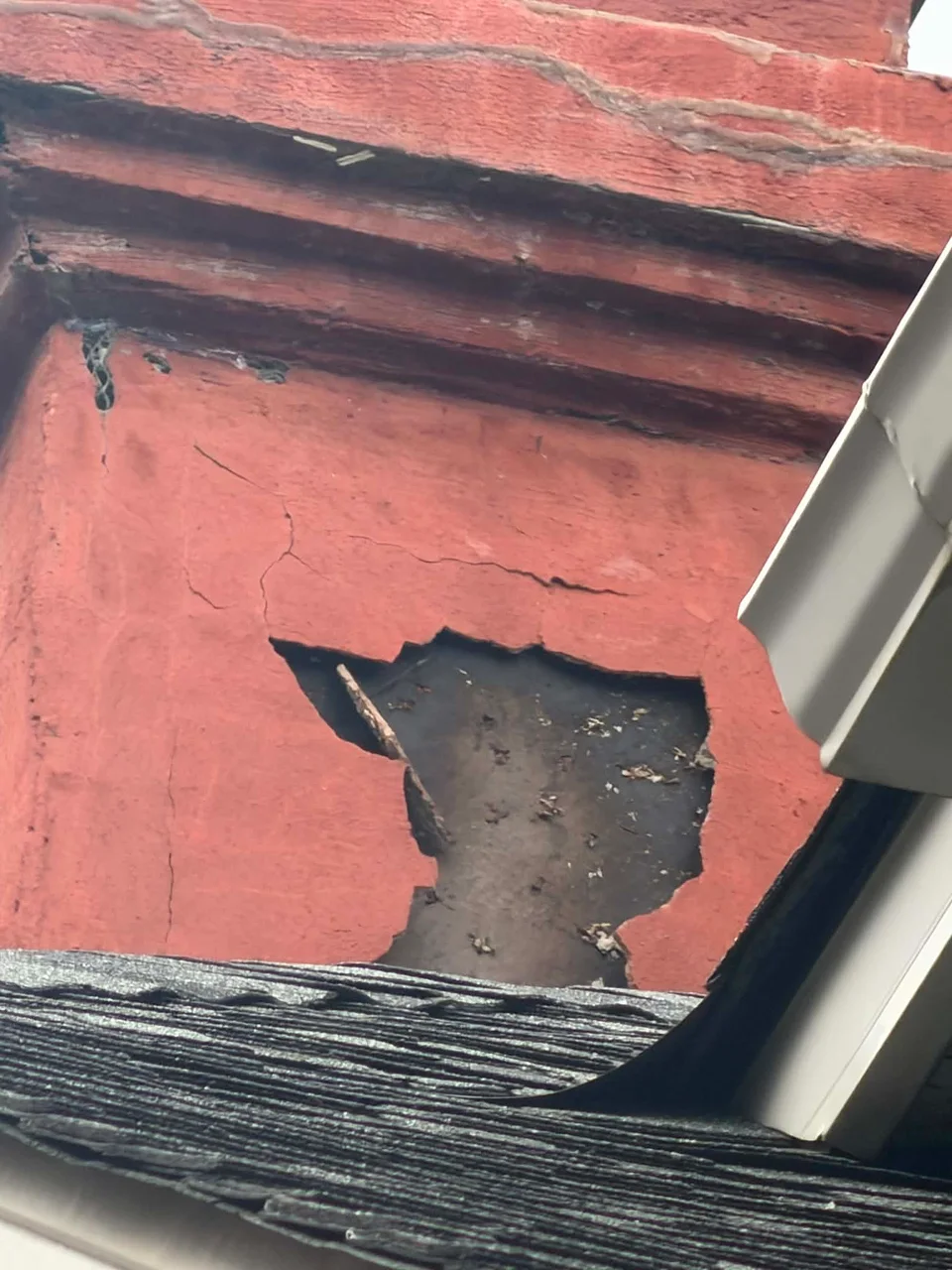 Close-up of a cracked red stucco chimney surface with a missing section.