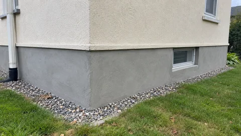AI-generated service illustration of light gray cement parging on an exposed house foundation.